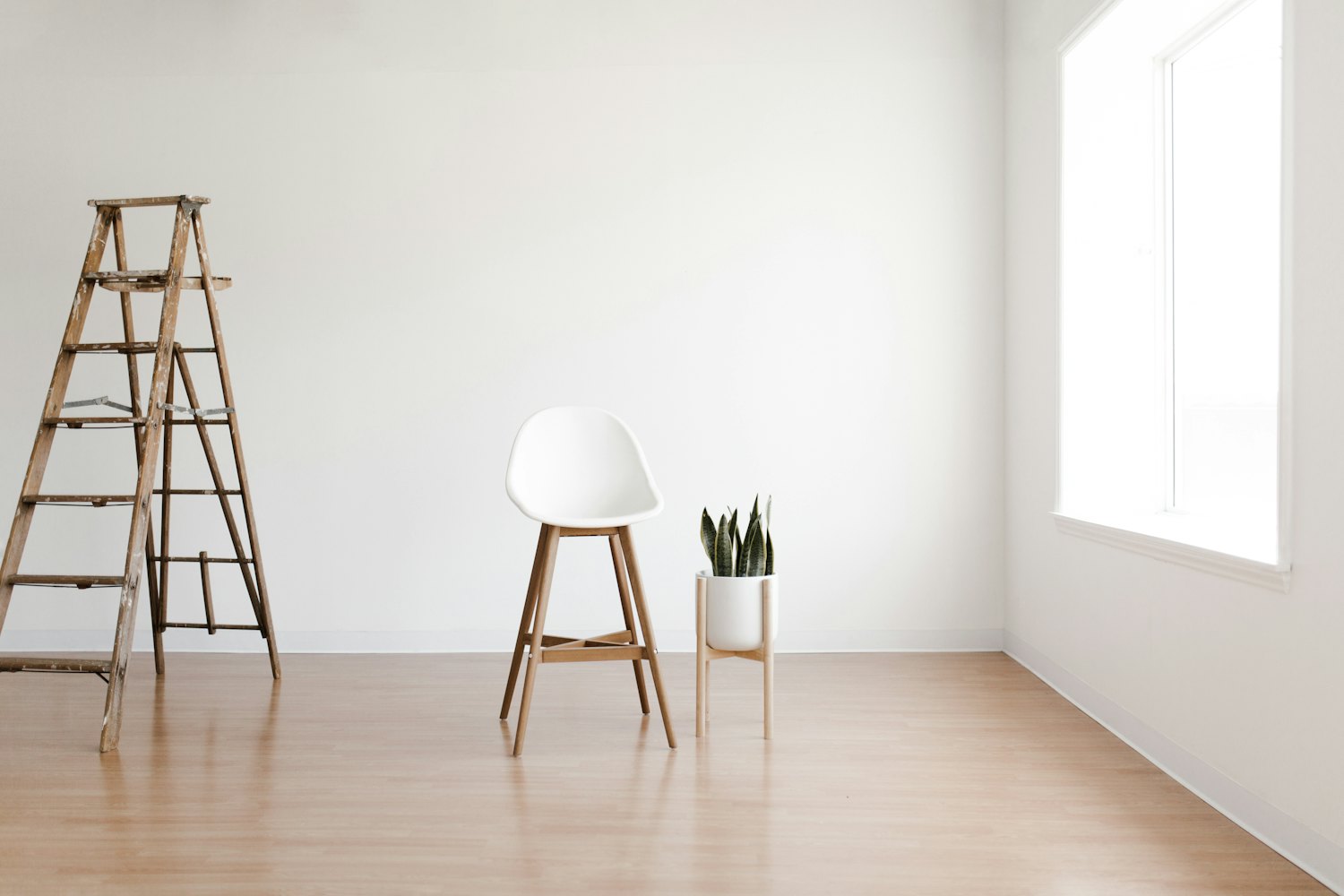 A freshly painted bright white room with a painter's ladder and a single chair