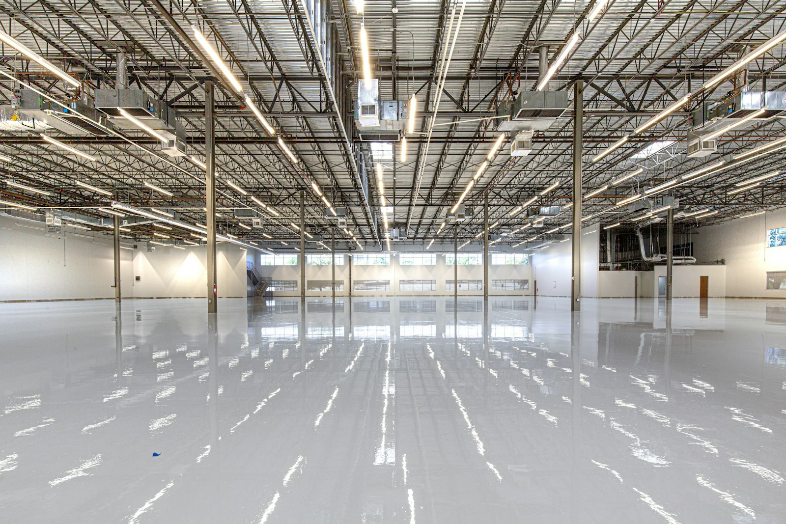 A vast commercial warehouse with a high-gloss light-grey floor mirroring the rows of overhead lights.